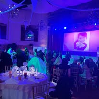 The lighting is purple and blue, and a large screen at the front displays a photo, likely part of a celebration or presentation.